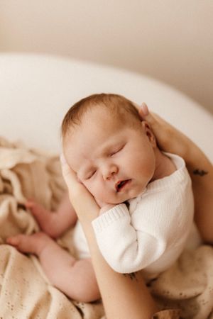 Sleeping newborn baby wearing white clothing nestled in soft beige blankets.
