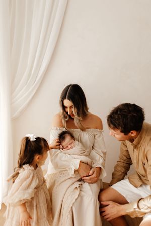 Family gathered together in tender moment with newborn baby in soft neutral setting.