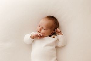 Peaceful newborn baby in white stretching while lying on white background.
