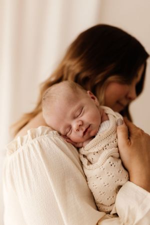 Sleeping newborn in knit sweater resting peacefully against caregiver.