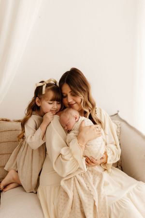 Intimate family portrait in soft beige tones sitting together on white couch.