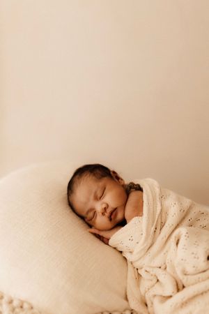 Peaceful newborn baby sleeps soundly wrapped in cream eyelet blanket.