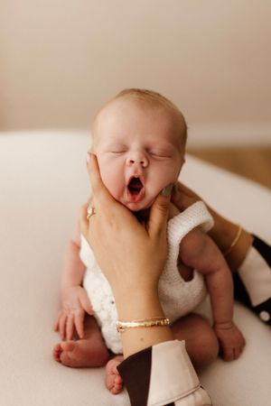Yawning baby in white knit outfit being gently held.