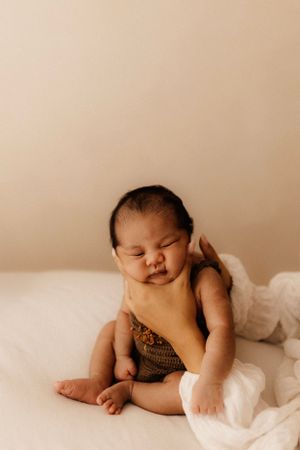 Baby in knit romper lounges on white bedding with peaceful expression.