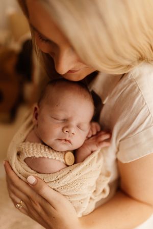 Intimate moment between mother and sleeping newborn wrapped in knit blanket.