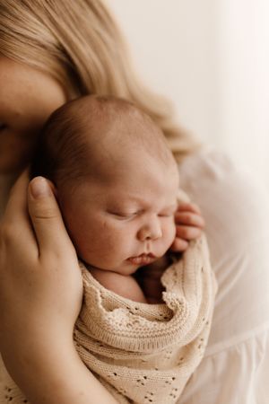 A sleeping newborn in a knit sweater nestles against someone in a tender moment.