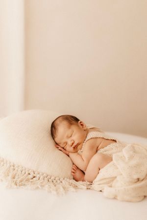 Newborn baby peacefully sleeping on white pillow draped in delicate cream knit blanket.