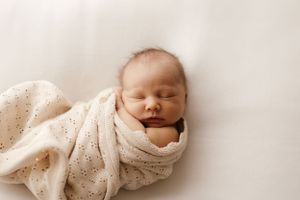 Peaceful newborn sleeping while swaddled in white textured wrap.