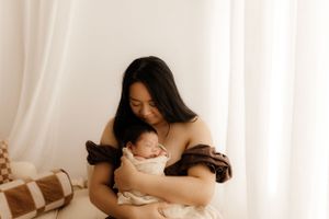 A tender maternal moment in warm sepia tones against white curtains.