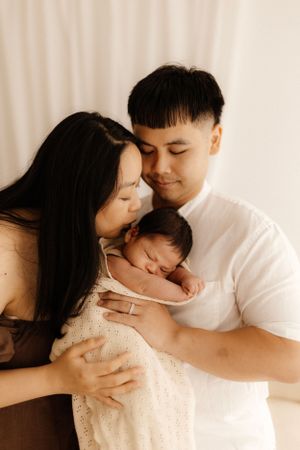 A heartwarming family portrait showing parents cradling their newborn in soft lighting.