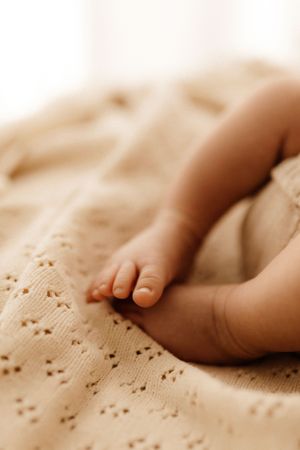 Close-up of tiny baby toes against textured cream-colored fabric in warm lighting.