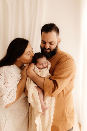 A tender family moment with parents embracing their newborn baby in warm neutral tones.
