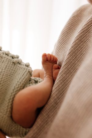 Close-up of tiny baby foot peeking out from grey knitted blanket.