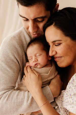 Tender family moment with sleeping newborn wrapped in beige knit sweater.