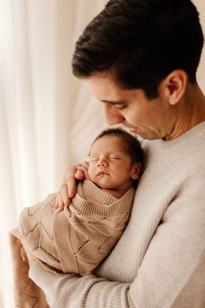 Close-up of sleeping baby in beige knit sweater cradled against parent.