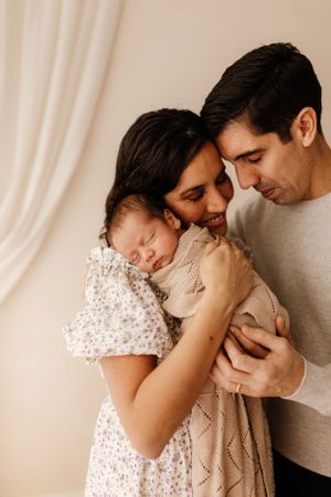Intimate family moment with sleeping newborn held close by parents in warm lighting.