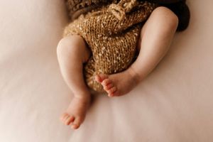 Close-up of baby legs and feet with brown knit clothing against white background.