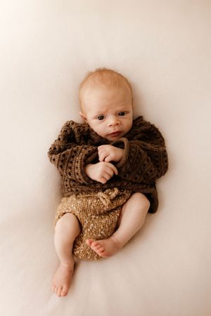 Baby wearing brown knit sweater laying on white background.