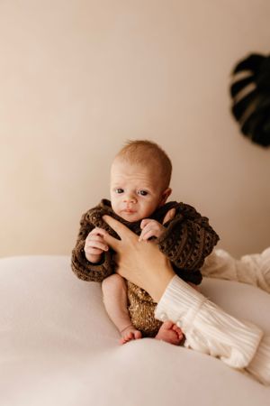 Baby in brown knit sweater on white surface with tropical leaf decor.