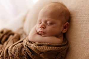 Peaceful newborn sleeping while wrapped in brown knitted blanket.