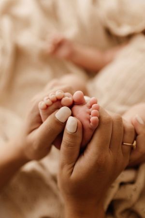 Close-up photo of tiny baby feet being gently held by hands with neutral nail polish.