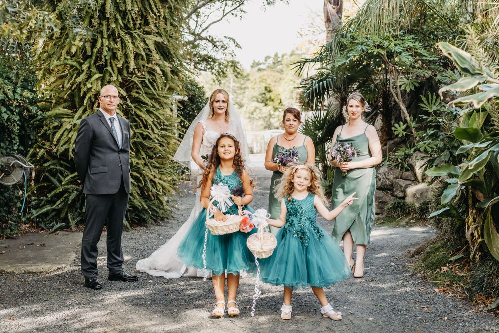 Wedding party with flower girls in turquoise dresses pose on garden path.