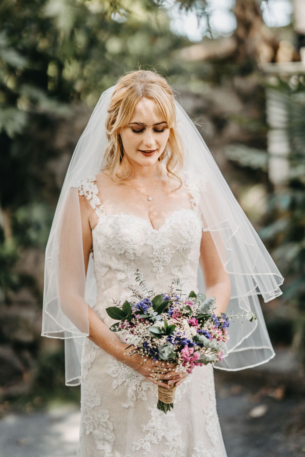 Bride looks down while holding colorful bouquet in garden setting.