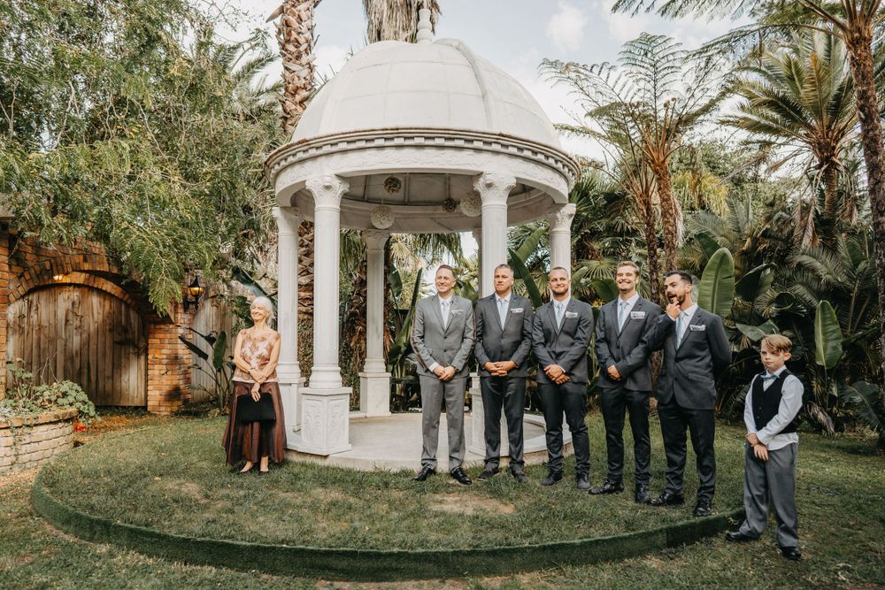 Wedding party stands under white gazebo surrounded by tropical palm trees during outdoor ceremony.