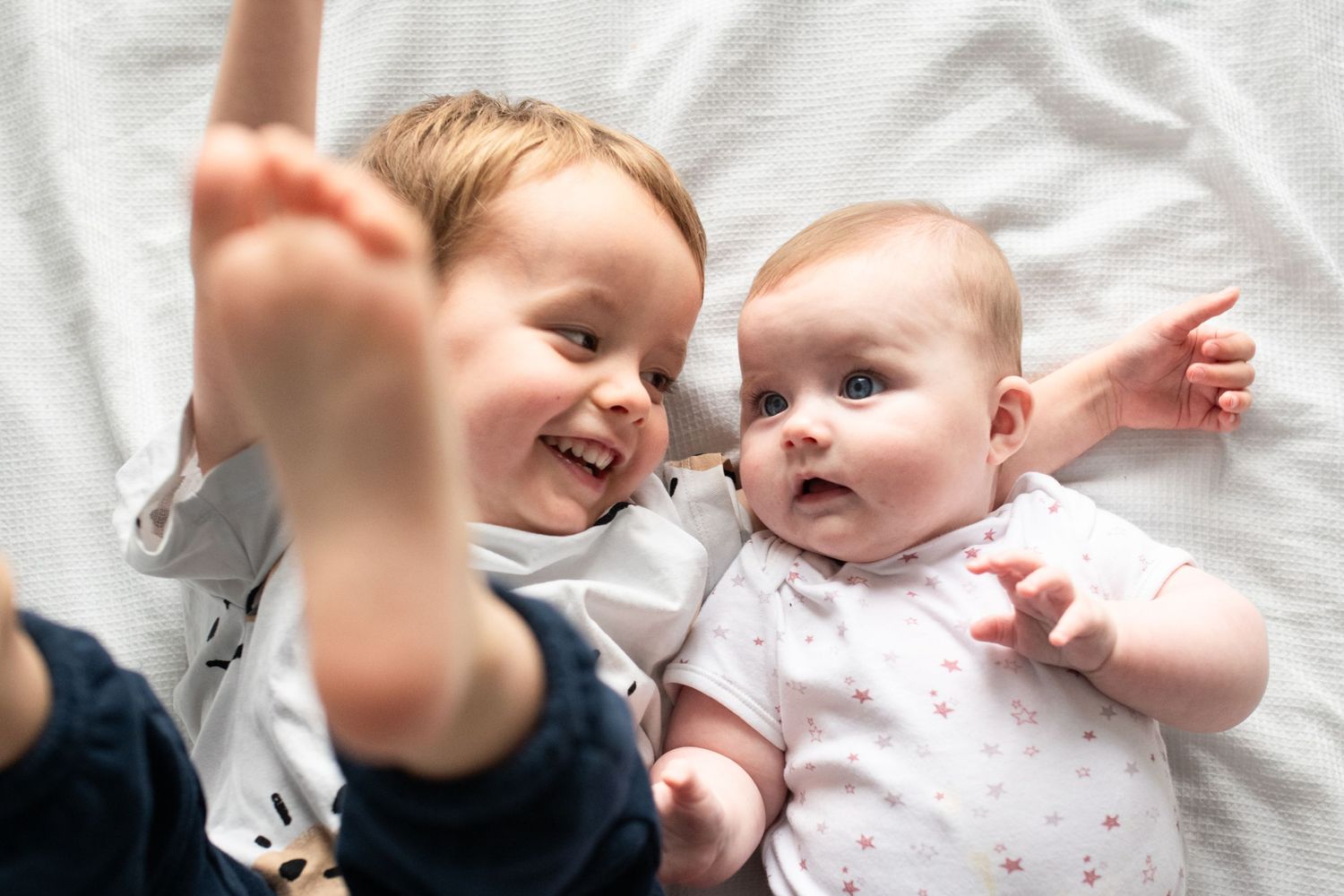 Newborn baby girl and her brother lying on the bed having snuggles, Sarah Frame Photography - Newborn - Surrey