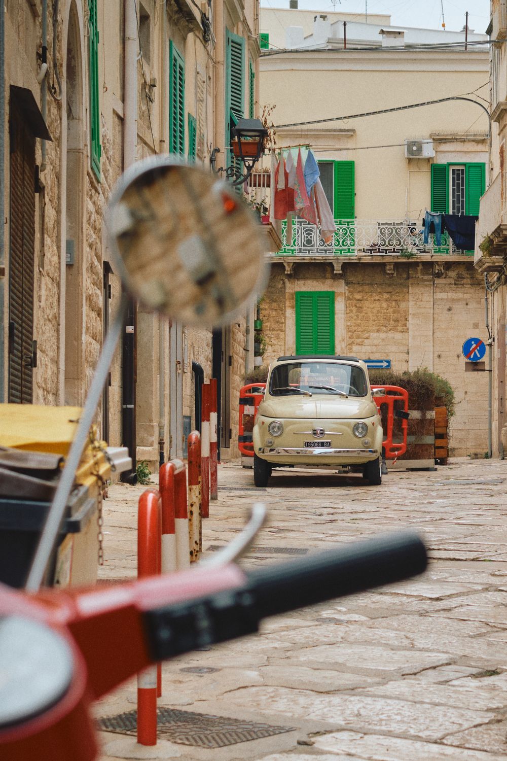 A vintage Fiat 500 parked on a cobblestone street with green shuttered buildings.