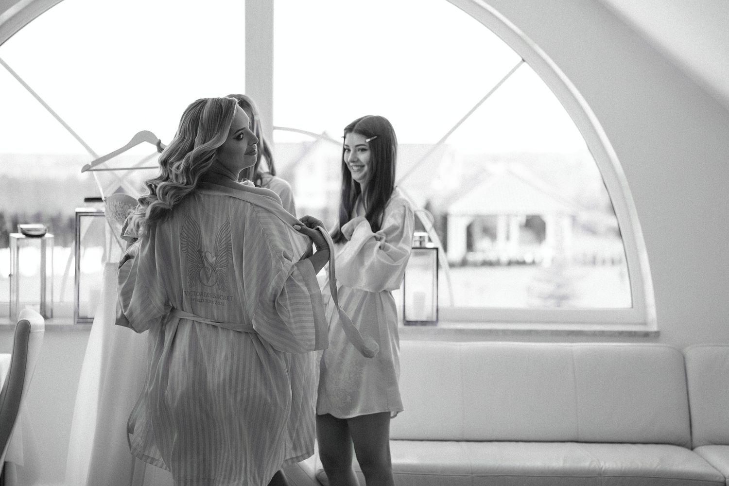 Two people in robes chatting by an arched window during wedding preparations.