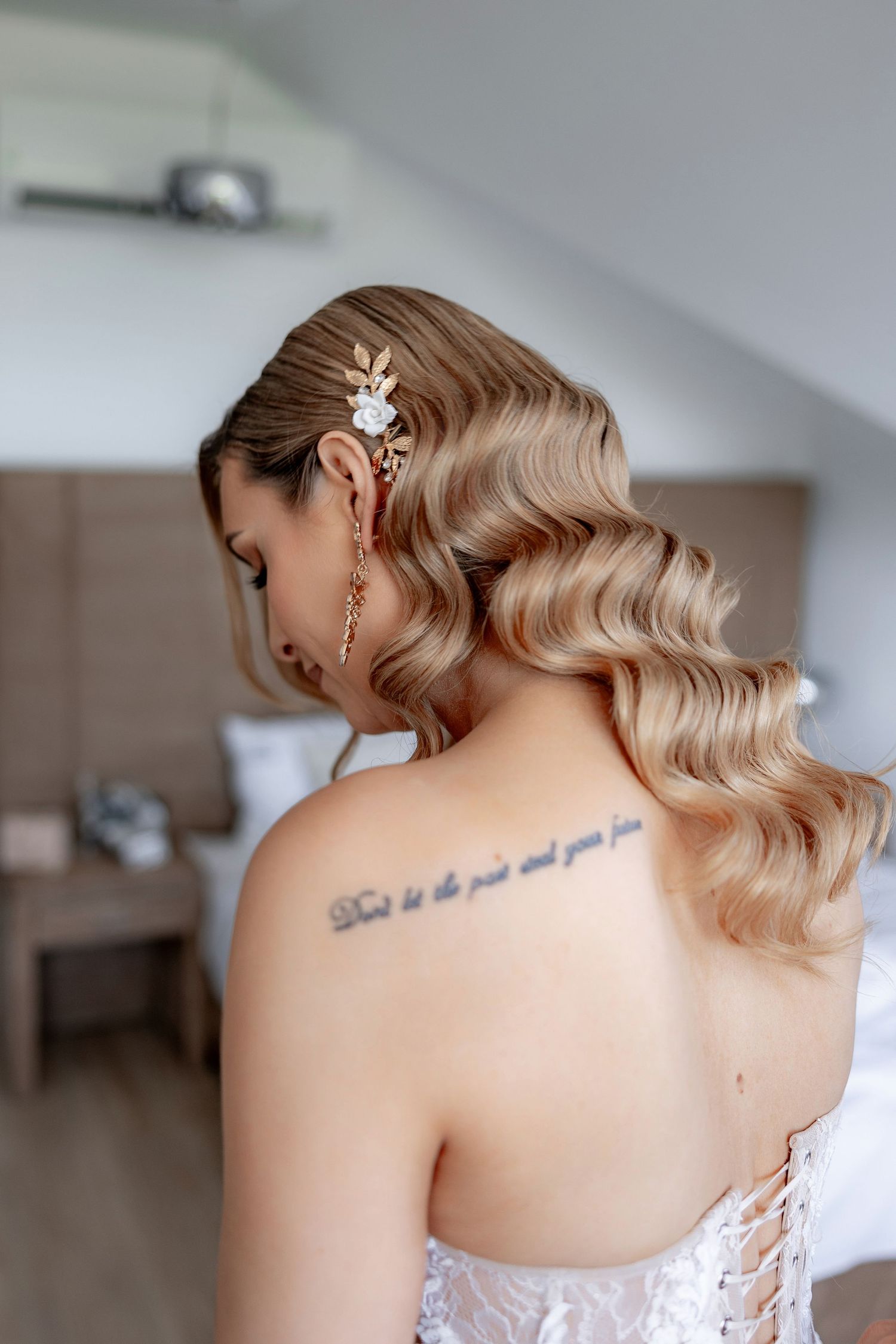 Elegant bridal hairstyle with vintage-inspired waves and decorative hair accessory showing a delicate back tattoo.