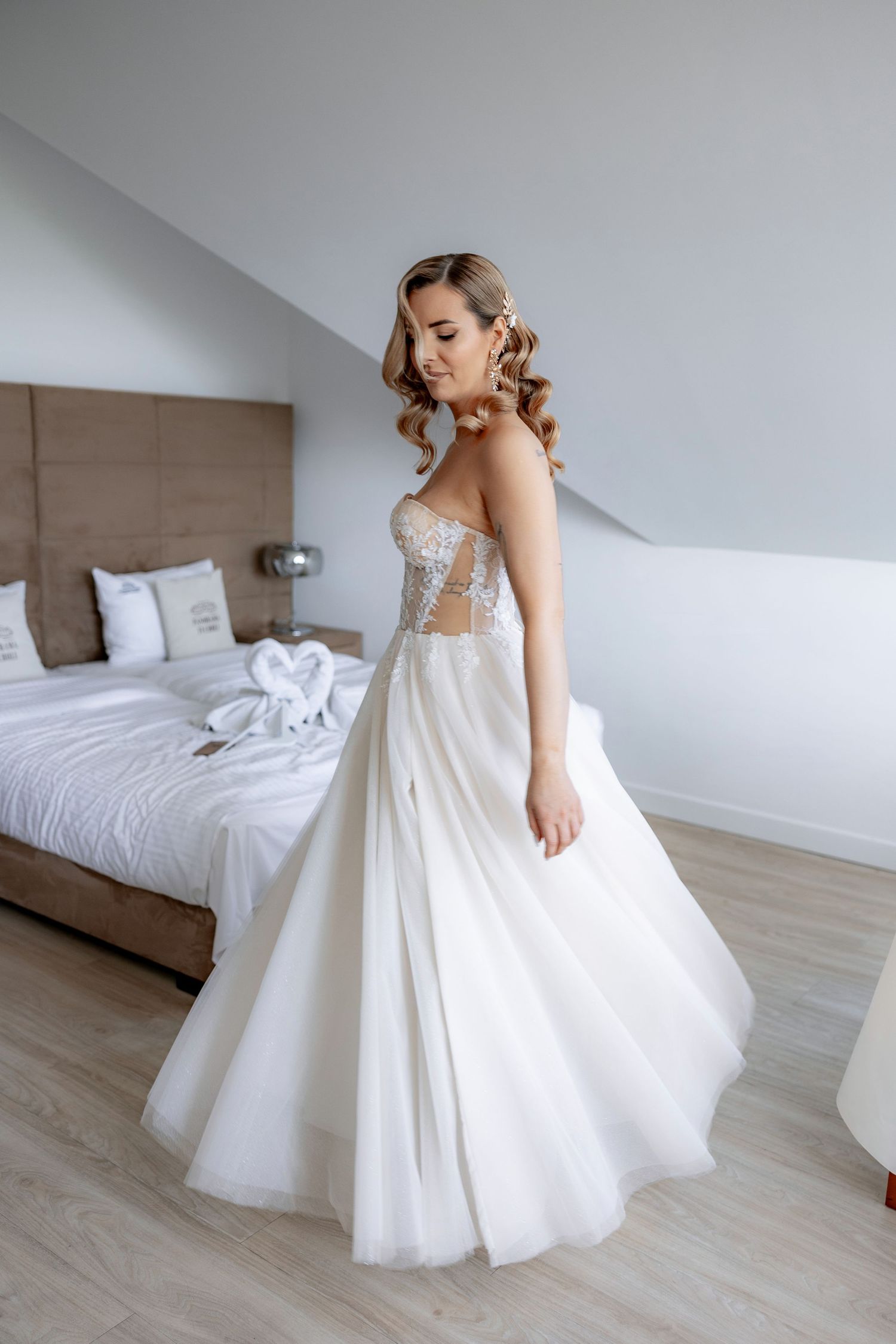 Elegant white wedding gown with lace corset bodice and flowing tulle skirt in a modern bedroom setting.