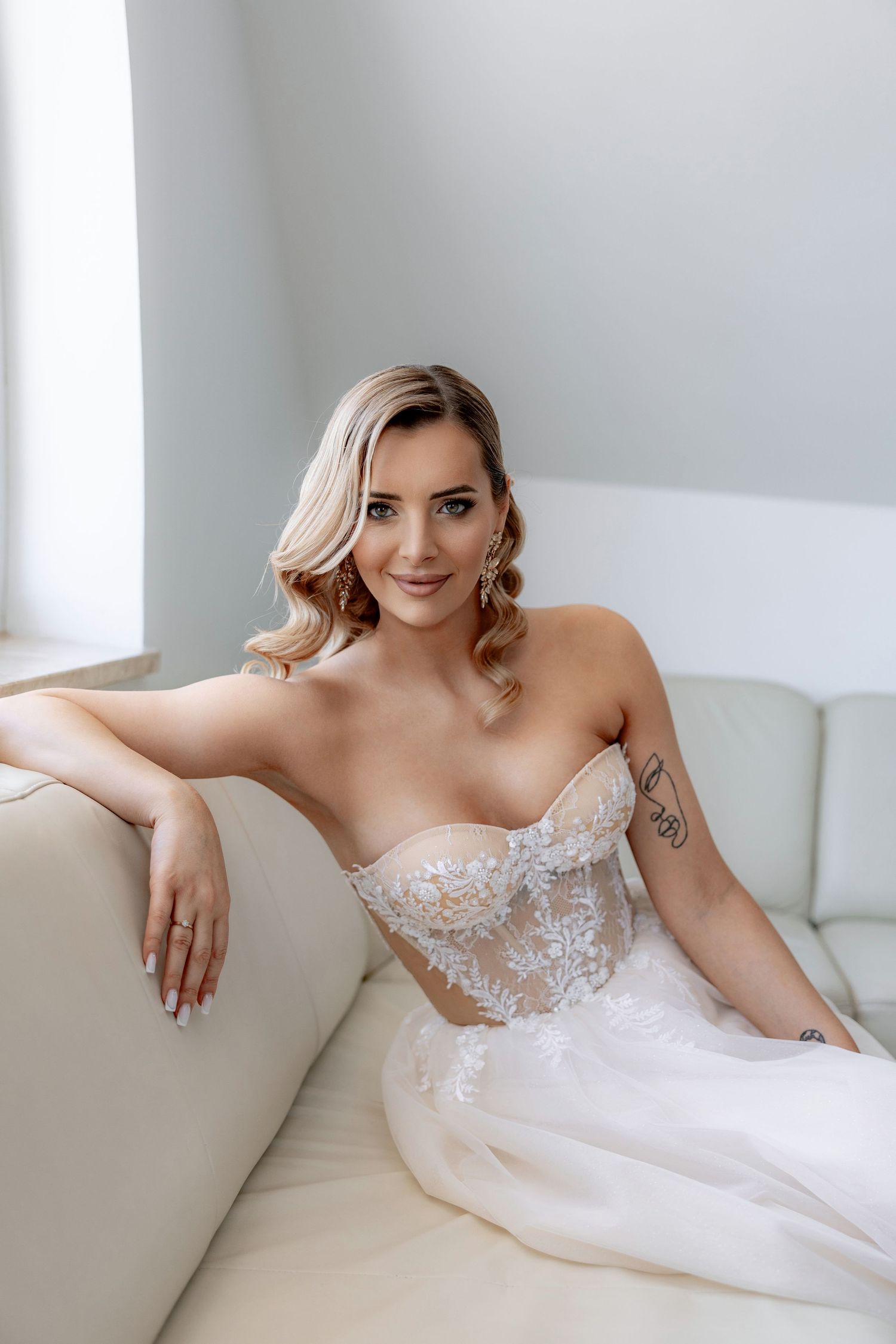 Elegant bridal portrait featuring a strapless lace wedding dress on a cream colored couch.