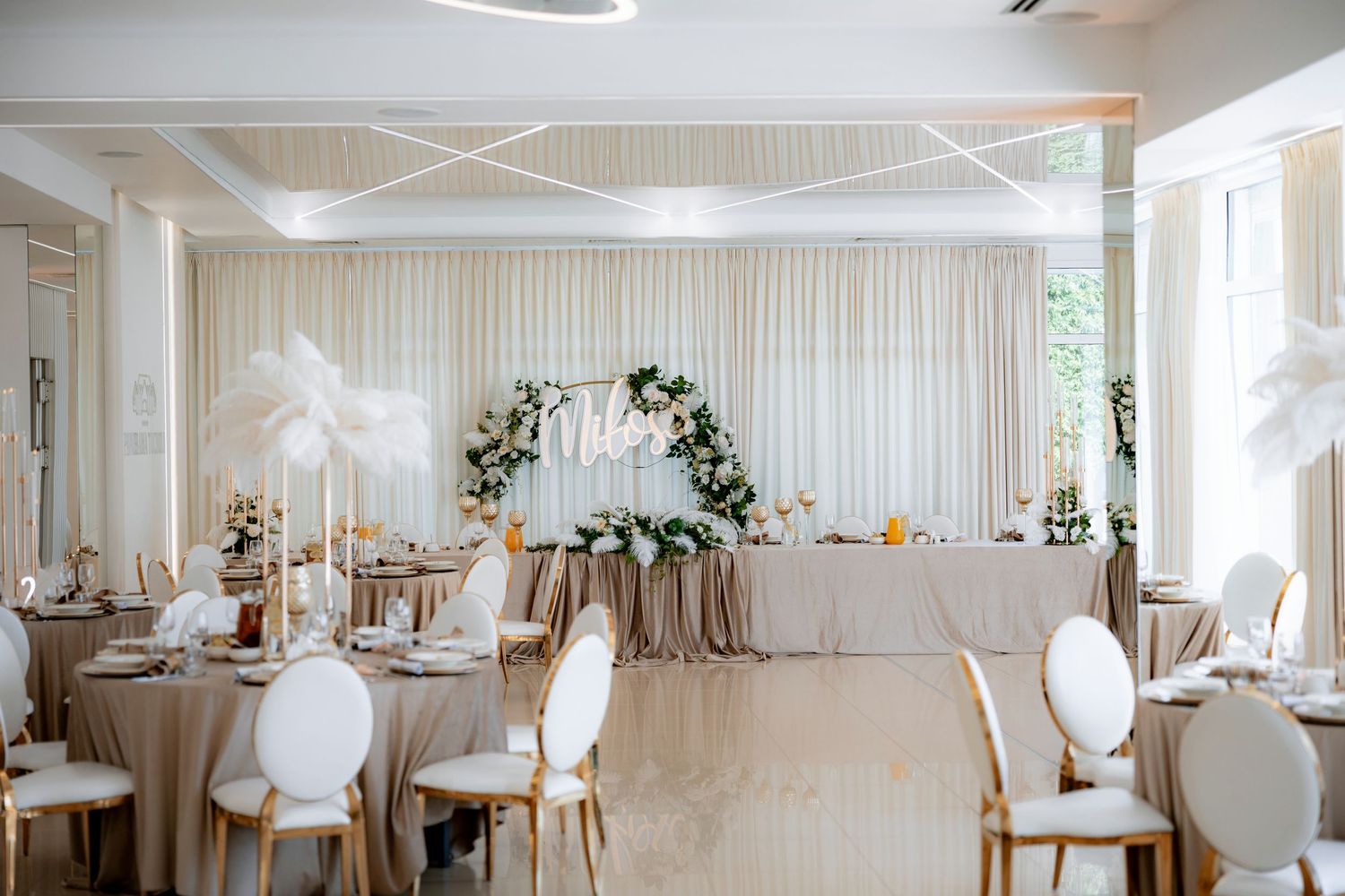 Elegant wedding reception setup with white draping, floral arch, and round tables with classic white chairs.