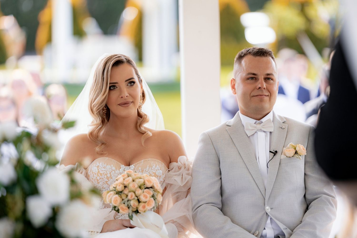 Elegant outdoor wedding ceremony under white gazebo with floral decorations.
