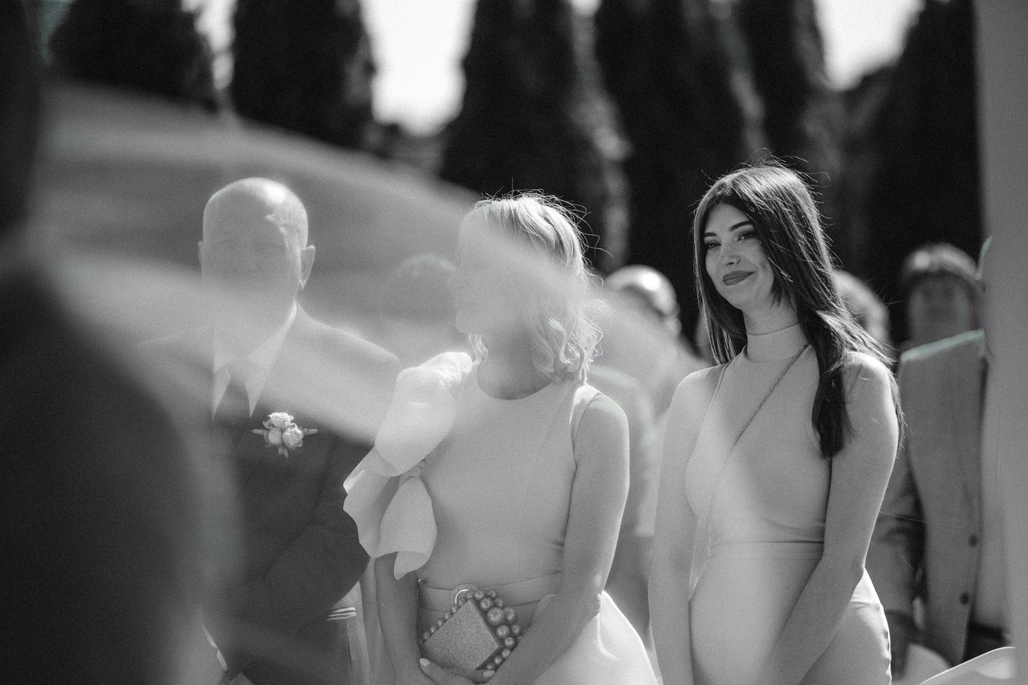 Black and white candid photo of wedding guests during an outdoor ceremony.