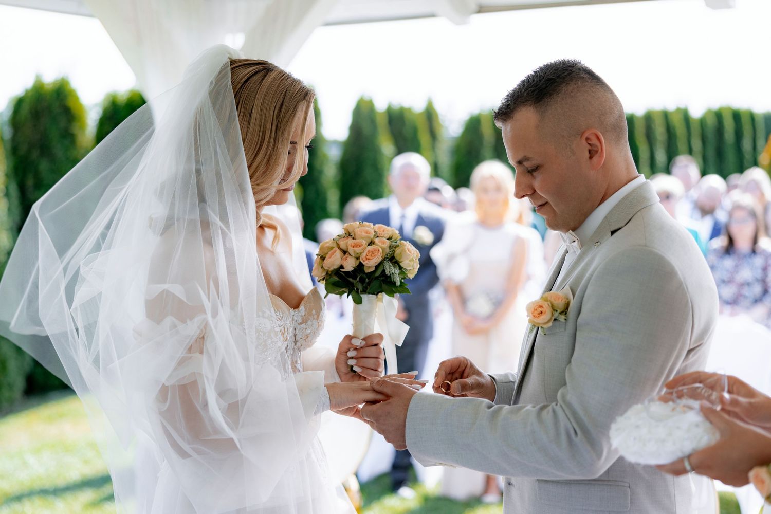 A tender moment during a wedding ceremony as a couple exchanges rings under a white canopy.
