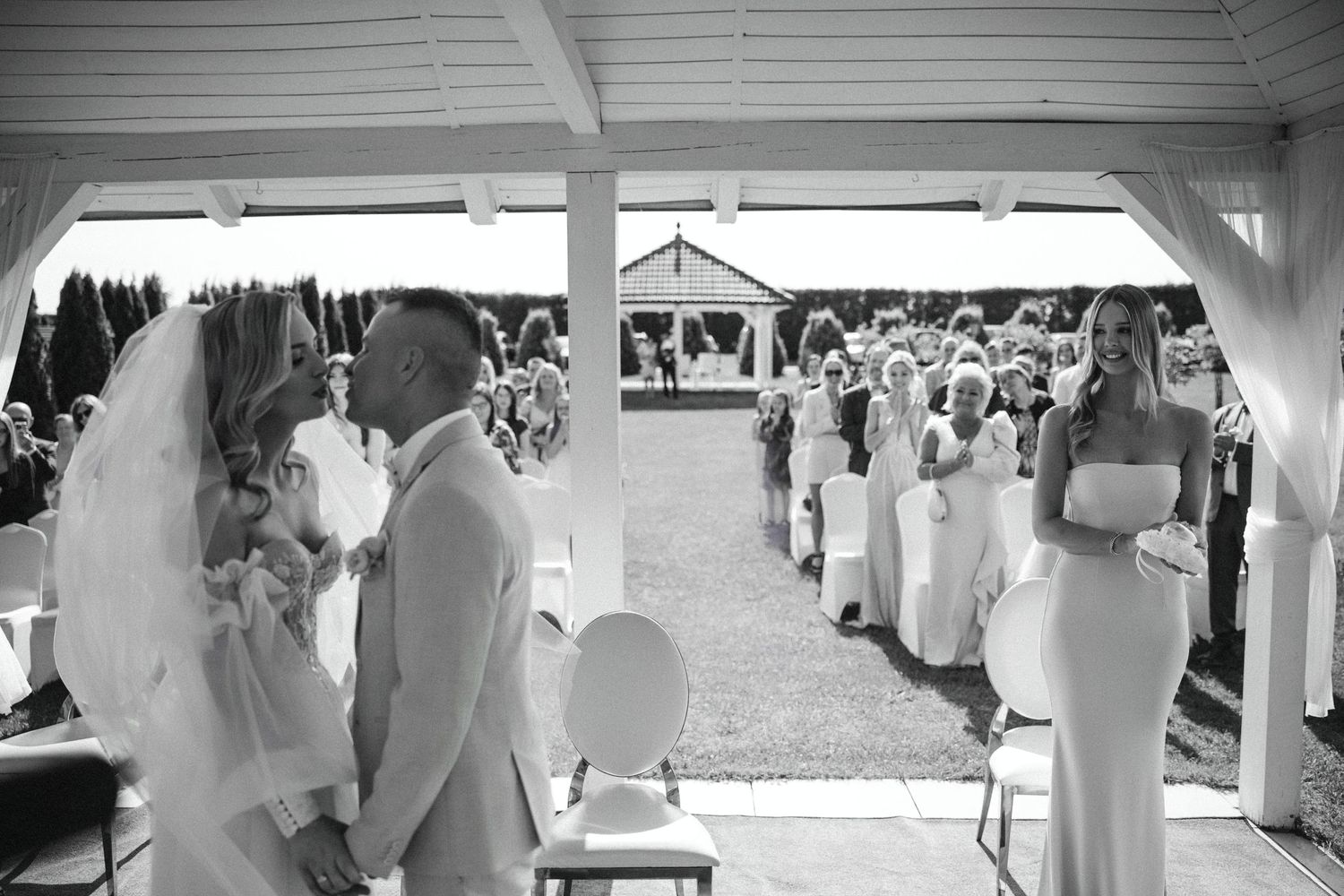 Wide-angle black and white shot of an outdoor wedding ceremony under a covered pavilion.