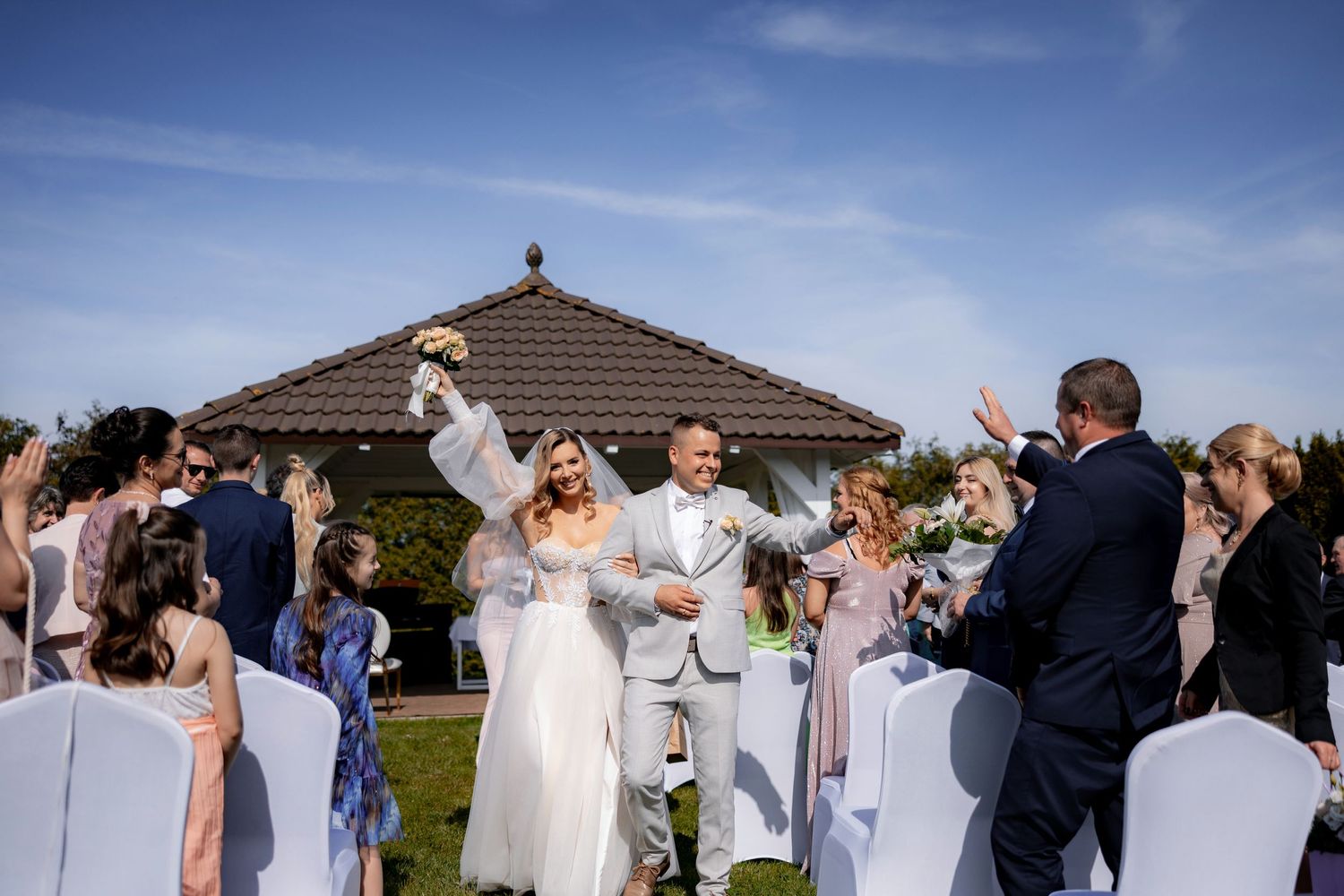 Outdoor wedding ceremony with guests celebrating under a blue sky and gazebo.
