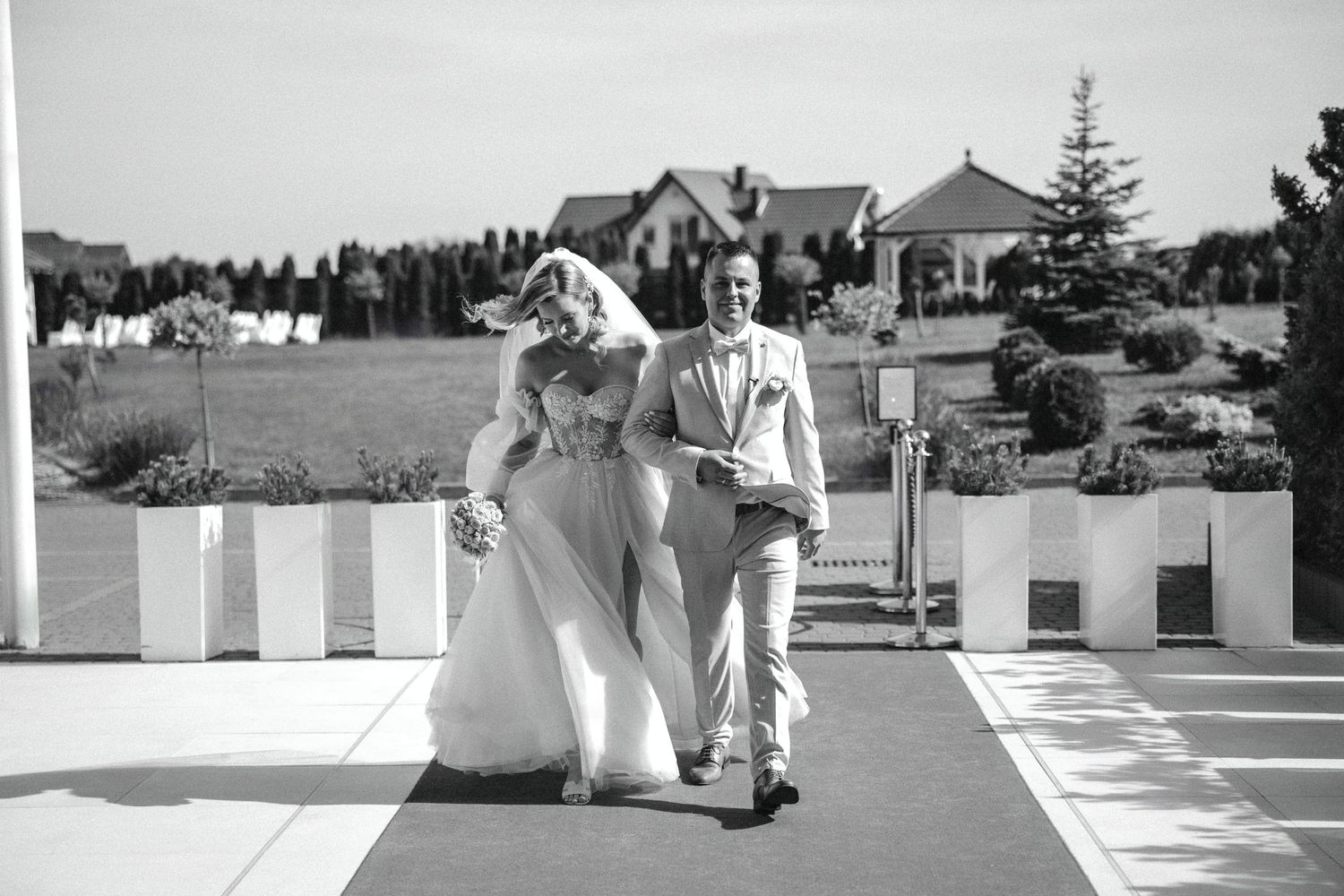 Black and white photo of a couple walking together on a checkerboard path.