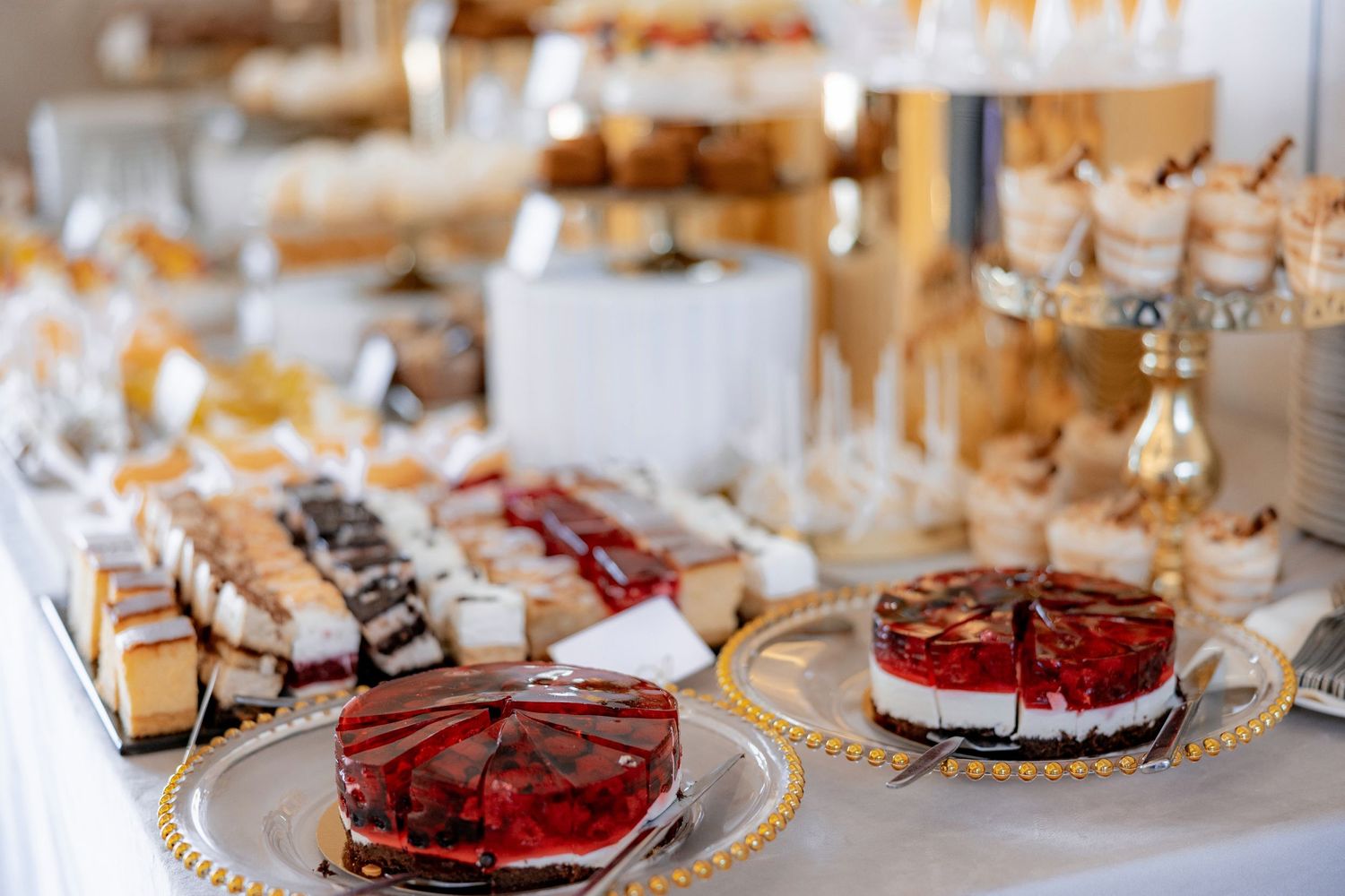 Elegant wedding dessert table with assorted cakes and treats on gold-rimmed plates.