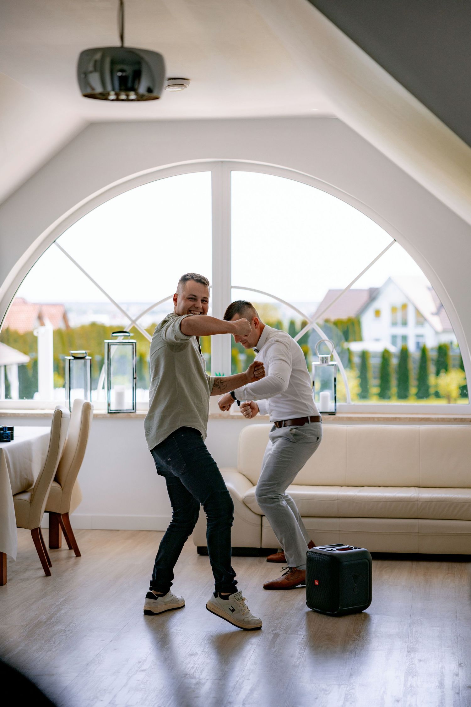 Two people dancing and having fun in a bright room with large arched windows.