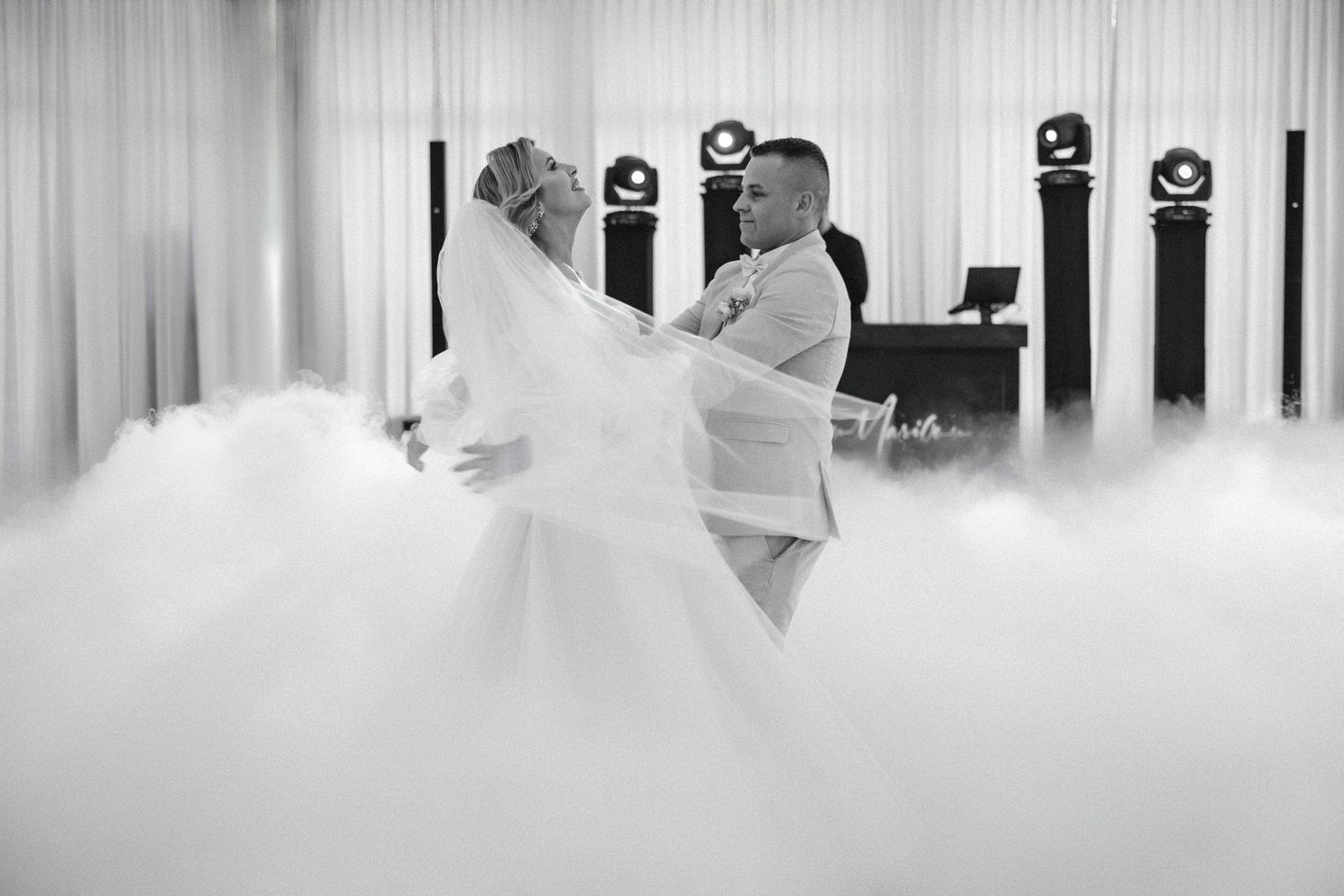 A romantic black and white capture of newlyweds dancing in swirling fog at their reception.