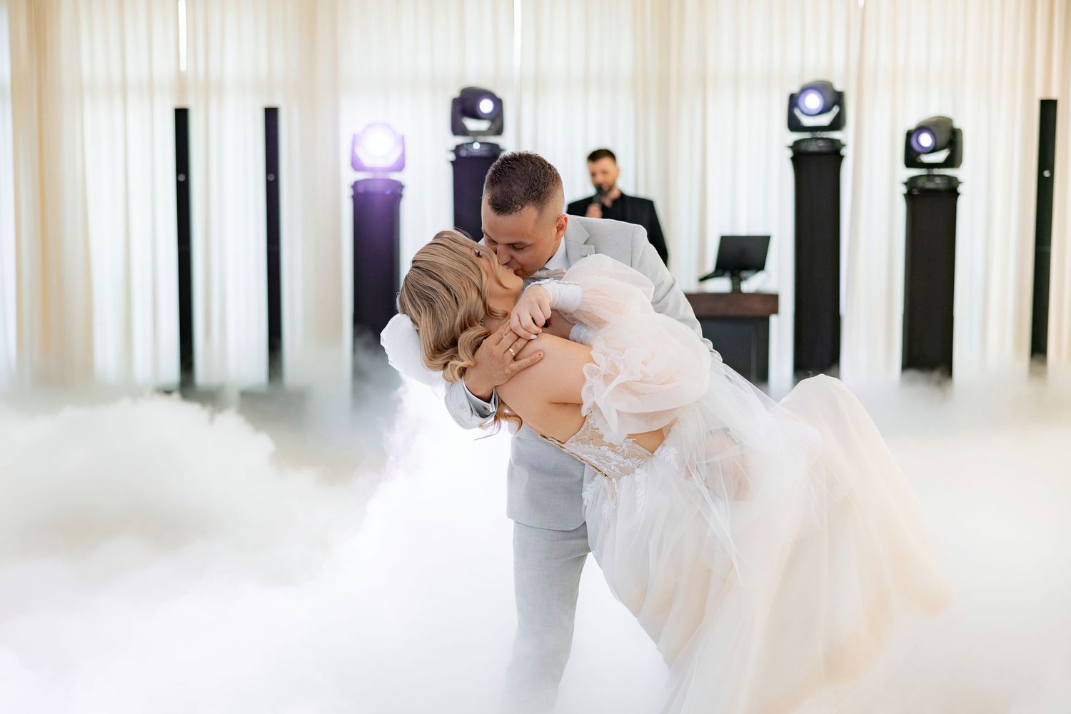 A couple shares their first dance surrounded by dramatic fog and uplighting at their wedding reception.