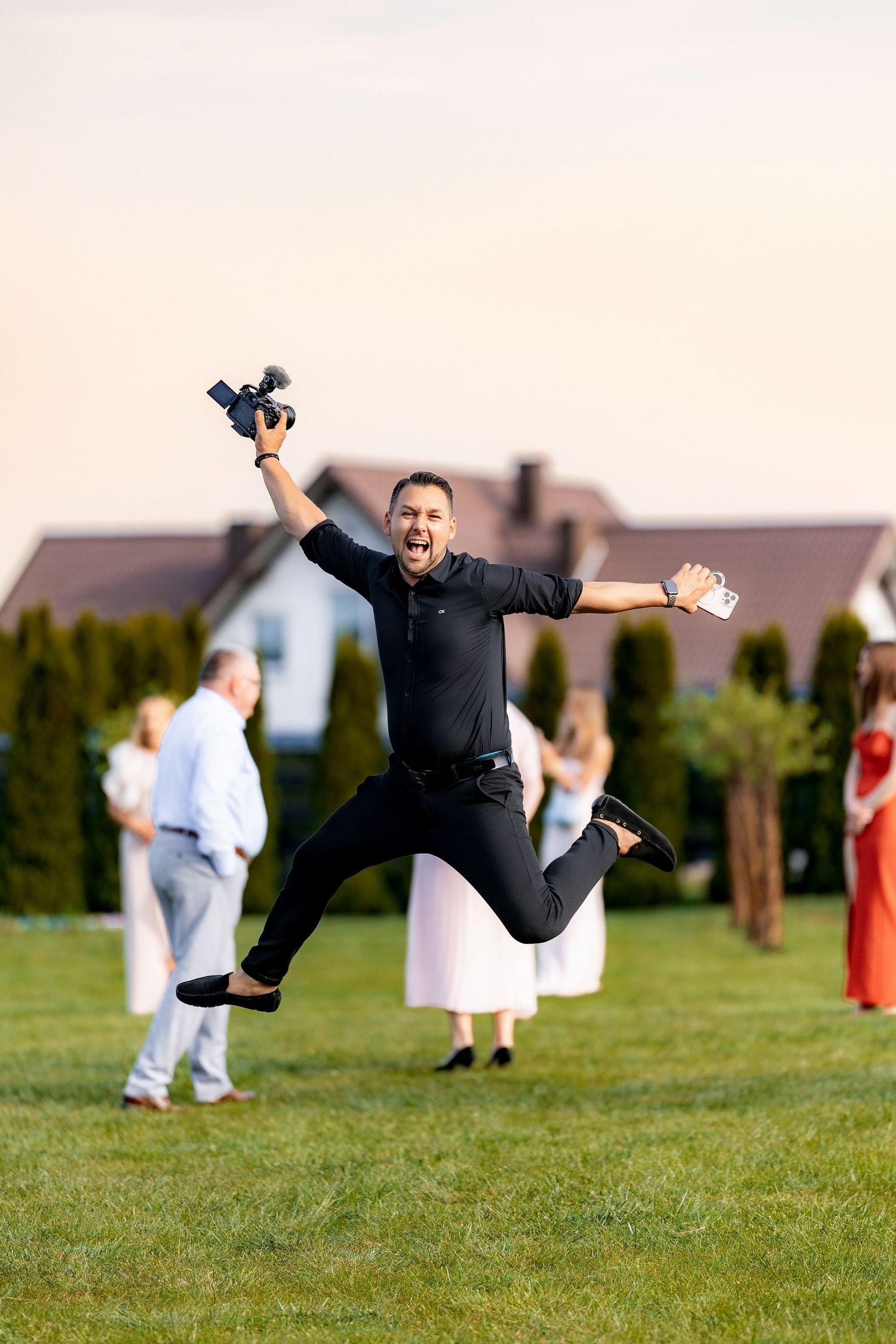 An enthusiastic wedding photographer jumps for joy while shooting outdoors on a sunny day.