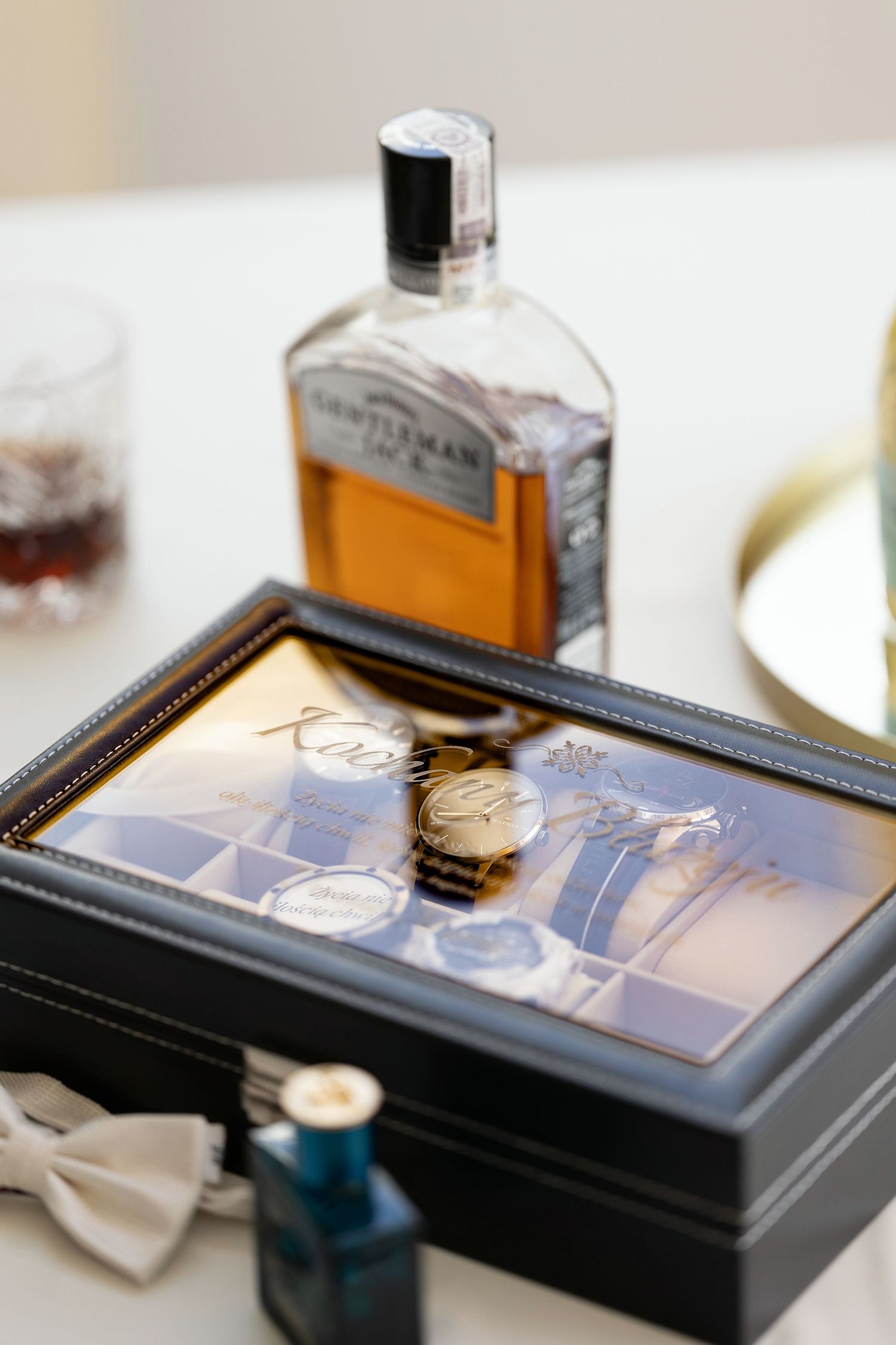 Wedding accessories including a watch, bow tie, and whiskey bottle arranged in a display box.