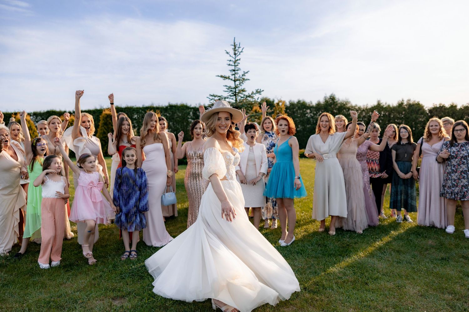 Wedding celebratory moment with guests cheering as bride twirls in a flowing white dress on a green lawn.