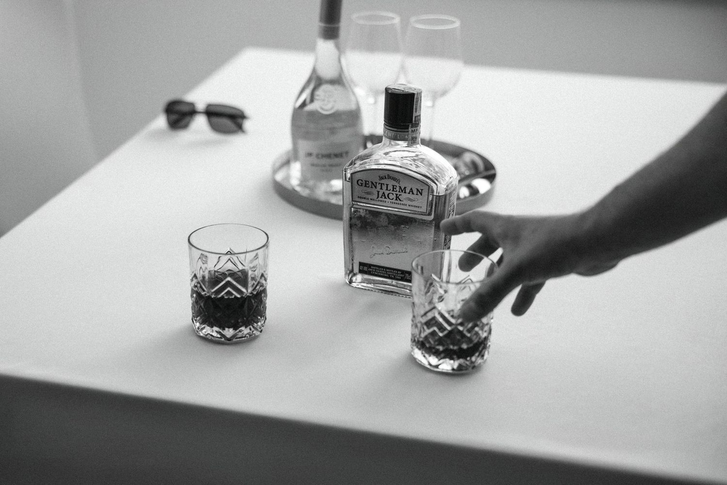 Black and white photo of whiskey being poured into crystal glasses.