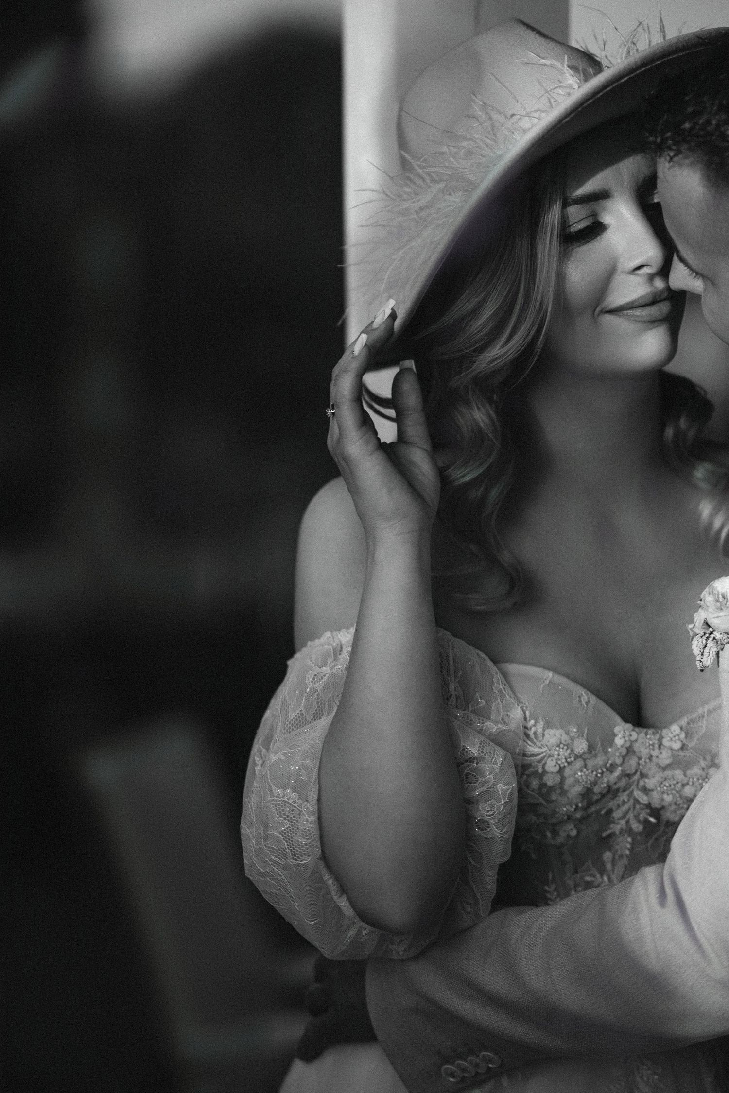 Intimate black and white portrait capturing a romantic bridal moment against a wall.